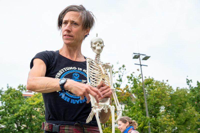 Somatischer Bewegungseinstieg, Heike Kuhlmann mit kleinem menschlichen Skelett zeigt Zusammenhänge im Knochenaufbau